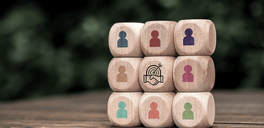 A stack of wooden blocks with printed people icons surrounding a central handshake icon